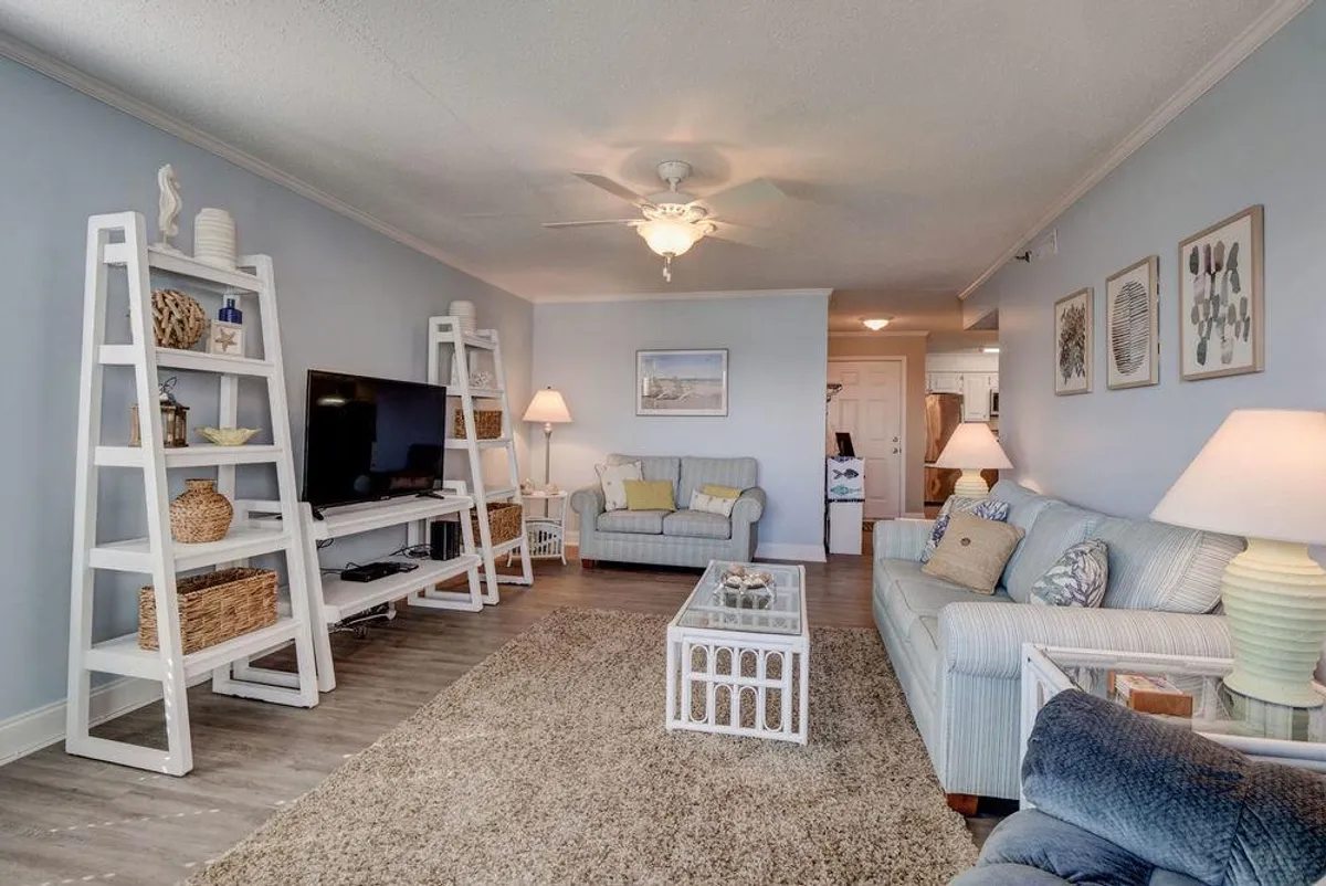 This image features an inviting living area with a soft-toned sofa, a coffee table, tasteful shelving with beach-inspired decor, and a warm lamp. The neutral color palette and decorative touches immediately evoke a sense of coastal calm, and the open space offers a glimpse into the overall layout of the living area beyond the entry.