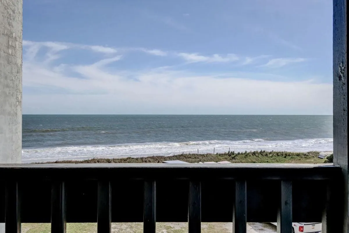 The image showcases a serene oceanfront view from a condo balcony, with the endless blue of the Atlantic meeting the sky. The sturdy balcony railing suggests a perfect spot to relax, while gentle sunlight and open vistas evoke tranquility and the allure of the sea breeze.