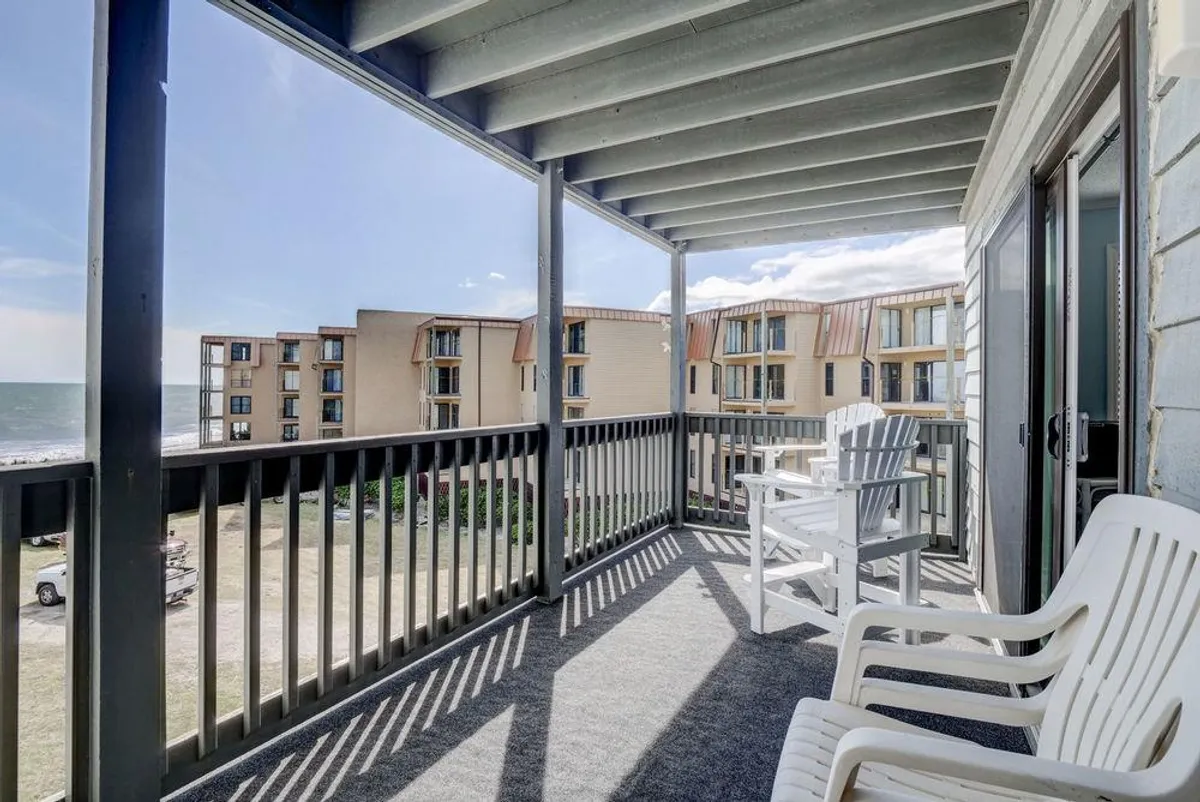 A private balcony with comfortable chairs overlooks the endless expanse of the Atlantic Ocean. The view captures gentle waves, a hint of surrounding buildings, and a tranquil sky, inviting relaxation at any time of day.