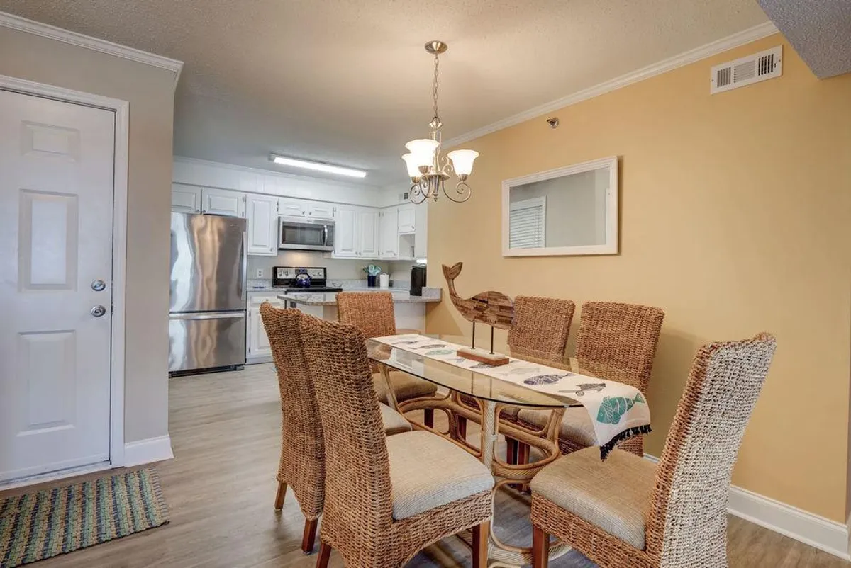 A view of the dining area, featuring a stylish dining table under a chandelier, with the kitchen visible in the background and decorative wall art adding warmth. The setup is perfect for sharing meals, celebrating special occasions, or gathering for board games.