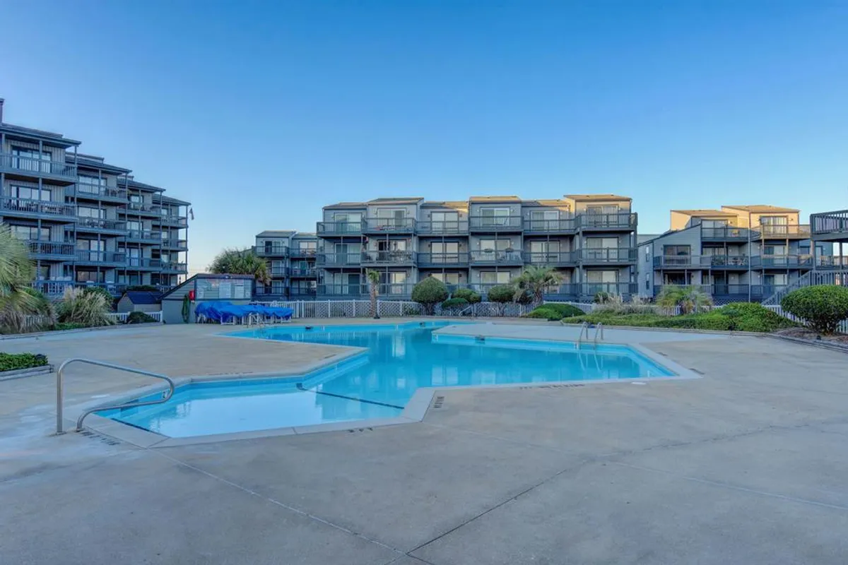 A sparkling swimming pool is surrounded by comfortable lounge chairs and lush landscaping, with the resort buildings in the background. The scene is inviting, suggesting both relaxation and opportunities for social gatherings, such as morning swims or evening poolside BBQs.