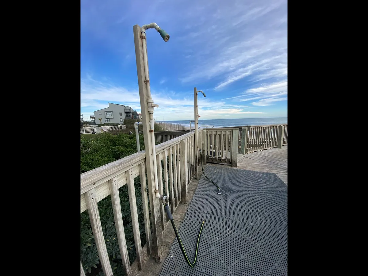 An exterior view of outdoor shower fixtures on a deck with a stunning backdrop of the ocean. The scene suggests the refreshing transition from beach play to relaxing on the private deck, with the ocean always in sight.
