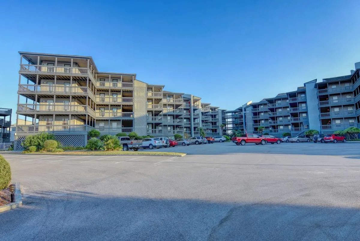 This image shows the exterior of apartment buildings with well-maintained landscaped areas and a parking lot. The scene suggests a communal outdoor space ideal for gatherings and activities, such as evening barbecues or casual socializing. Families and friends could easily envision enjoying meals together outside, supported by the presence of grills and open areas.