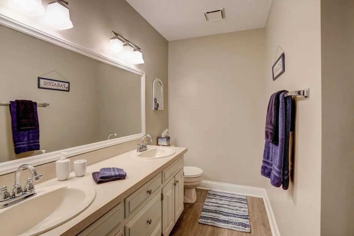 A spa-inspired bathroom featuring a double sink vanity with a large mirror above, neatly arranged towels, and a toilet. The palette is soothing and fresh, evoking a sense of calm. The design promotes relaxation and offers ample space for personal routines, aligning with the 'refresh and rejuvenate' promise of the section.
