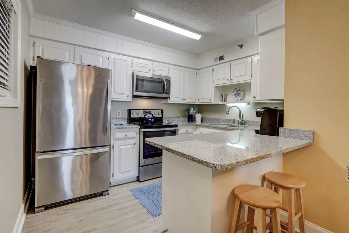 A modern kitchen scene highlighting stainless steel appliances, a granite countertop, and comfortable bar stools. The breakfast bar is inviting for quick morning coffee or a casual snack, seamlessly connecting the kitchen to the living area.