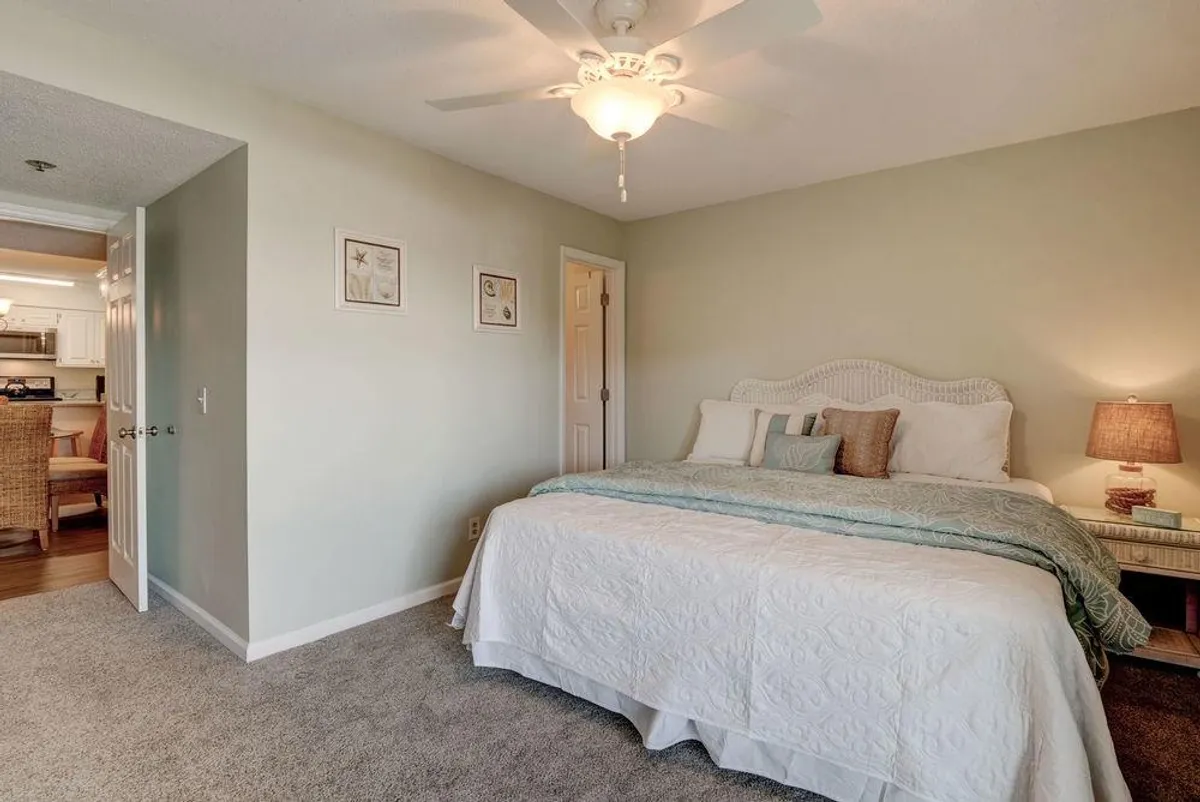 A tranquil master bedroom highlighted by a king-sized bed adorned with decorative pillows and soft bedding. Gentle sunlight streams in, illuminating the serene space. Beside the bed is a nightstand with a lamp, and above it, coastal-inspired wall art with a starfish motif. The mood is peaceful and inviting, ideal for rest and private relaxation.